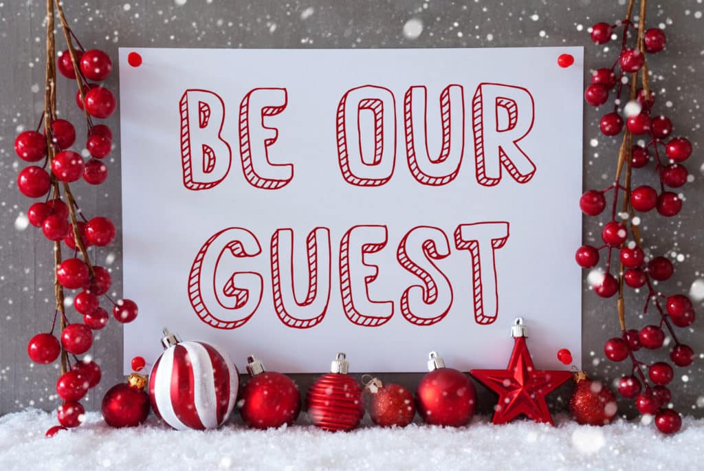 A sign decorated with red Christmas baubles that says 'Be Our Guest'