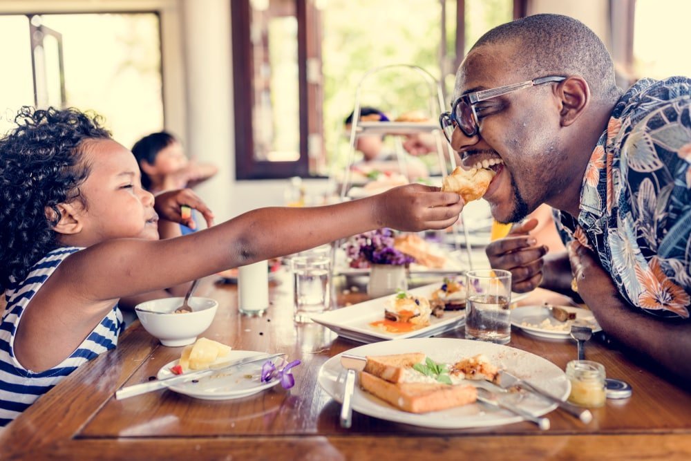 A child feeding her dad pastry across the table