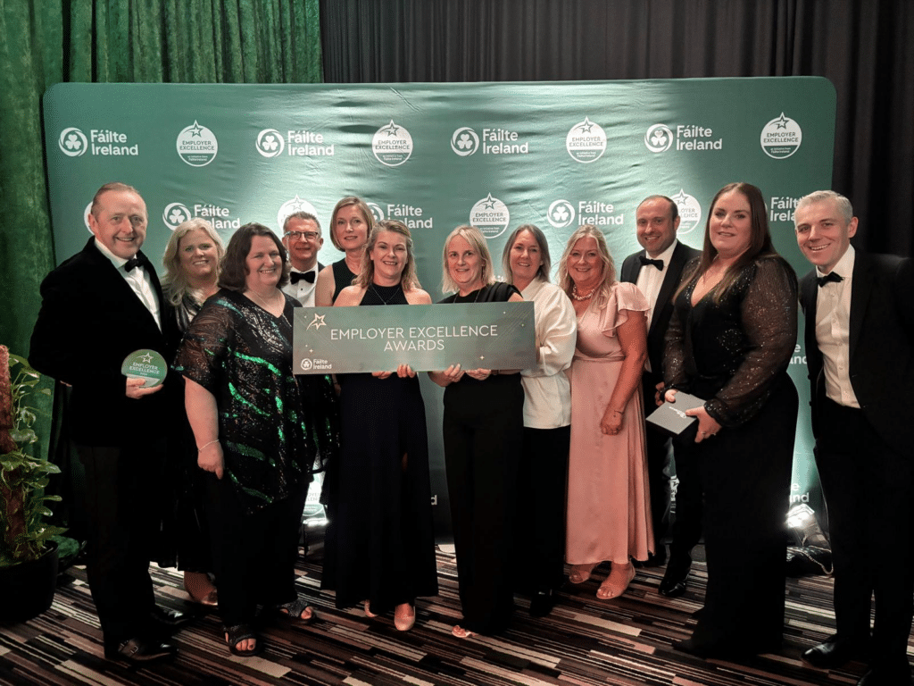 Picture of the PREM Hospitality team holding awards and celebrating their win. There are 13 people in the image in formal wear.