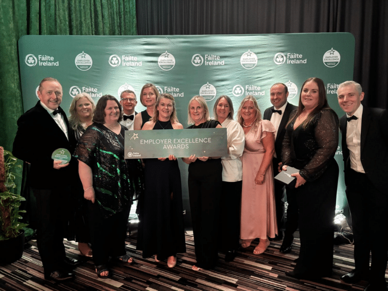 Picture of the PREM Hospitality team holding awards and celebrating their win. There are 13 people in the image in formal wear.